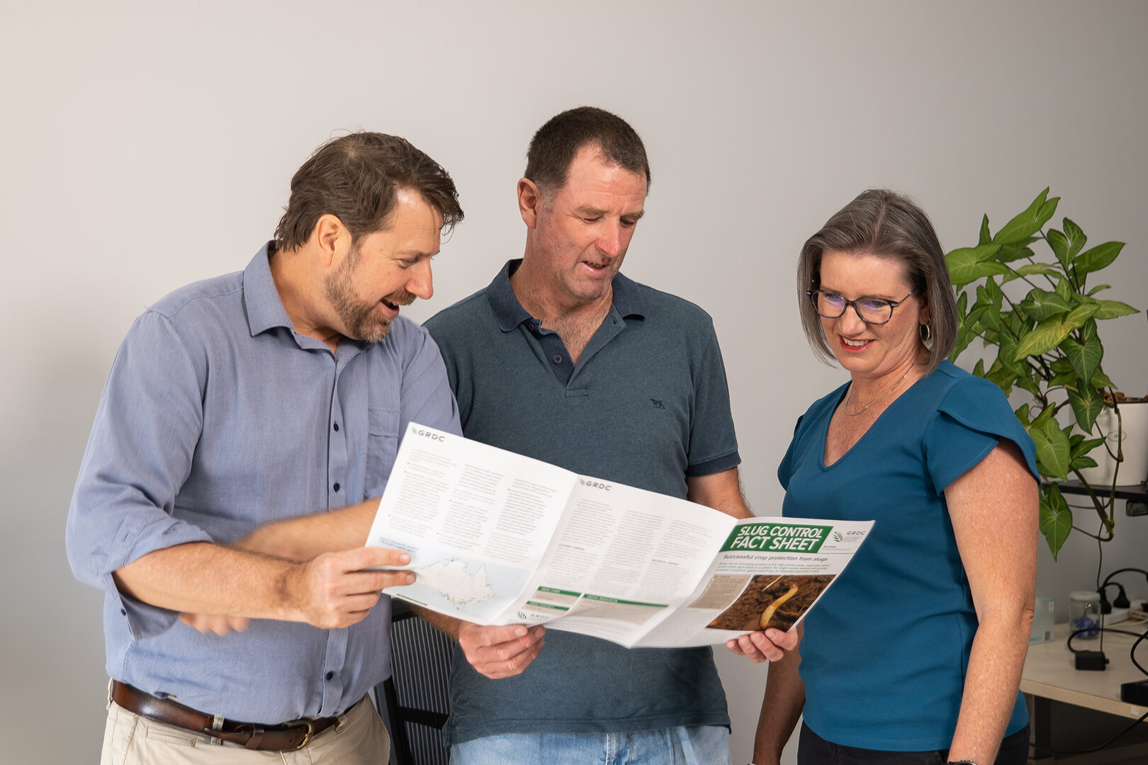 Majella, Paul, and Keith stand together in an office, looking at a pamphlet