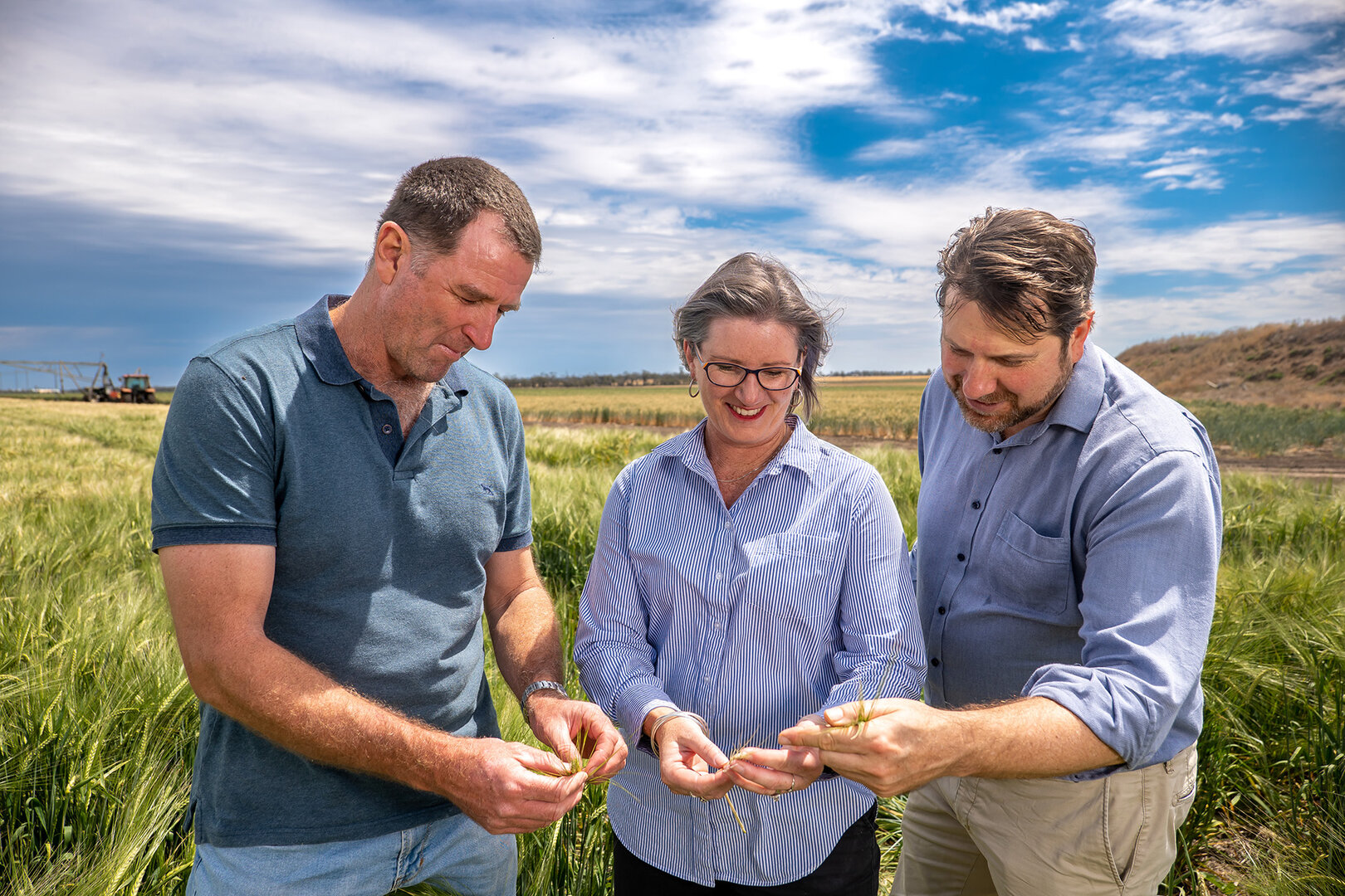 Majella, Paul, and Keith stand together in a field looking closely at their crops. Majella is holding some in her hand.